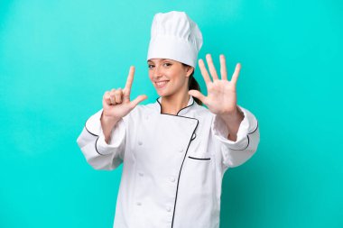 Kafkasyalı genç aşçı kadın mavi arka planda izole edilmiş yediyi parmaklarıyla sayıyor