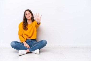 Beyaz duvarda tecrit edilmiş beyaz bir kadın yerde oturuyor. Parmaklarıyla beşi sayıyor.