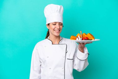 Mavi arka planda mutlu bir ifadeyle izole edilmiş waffle tutan Kafkasyalı aşçı kadın.