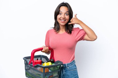 Elinde yiyecek dolu bir alışveriş sepeti tutan genç bir kadın telefon jesti yapıyor. Bana geri dönüş işareti ver.