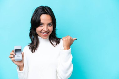 Young hispanic woman holding a engagement ring isolated on blue background pointing to the side to present a product clipart