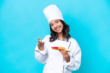 Mavi arka planda saşimi tutan genç İspanyol aşçı kadın iyi bir anlaşma için el sıkışıyor.