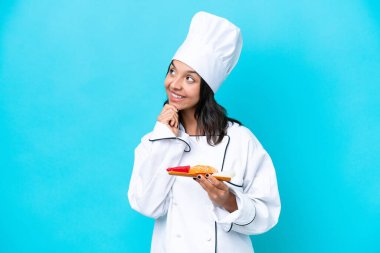 Genç İspanyol aşçı kadın elinde saşimi tutarken mavi arka planda izole edilmiş gülümserken yukarı bakıyor.
