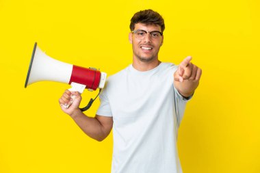Sarı arka planda izole edilmiş, elinde megafonla gülümseyen beyaz, yakışıklı genç bir adam.