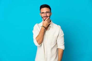 Kafkasyalı genç adam mavi arka planda izole edilmiş. Şüpheleri var.
