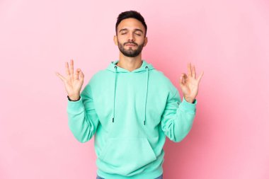 Zen pozisyonunda pembe arka planda izole edilmiş genç beyaz bir adam.