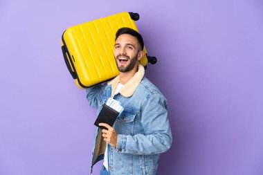 Kafkasyalı genç adam mavi arka planda izole edilmiş, bavul ve pasaportla tatilde.