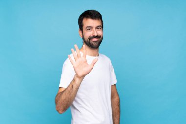 Mavi arka planda sakallı genç adam parmaklarıyla beşi sayıyor.