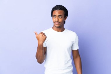 Örgülü genç Afrikalı Amerikalı bir adam mor arka planda izole edilmiş bir adam bir ürünü sunmak için yan tarafı işaret ediyor.