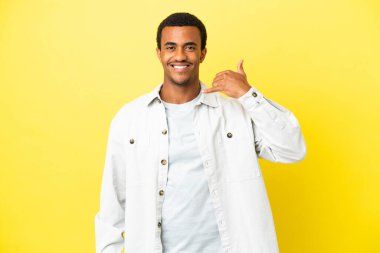 Sarı arka planda yaşayan Afro-Amerikalı yakışıklı bir adam telefon jesti yapıyor. Bana geri dönüş işareti ver.