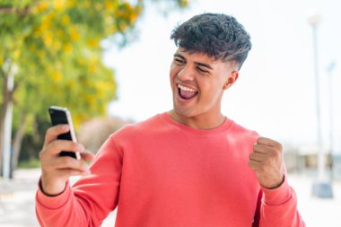 Dışarıda cep telefonu kullanan ve zafer jesti yapan genç bir İspanyol.