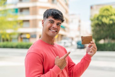Genç İspanyol bir adam açık havada bir cüzdan tutuyor ve ona doğrultuyor.