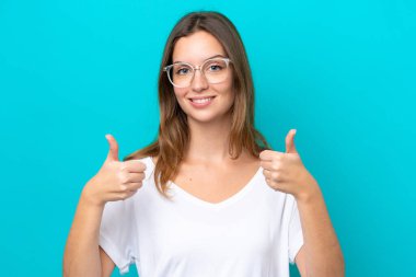 Mavi arka planda, gözlüklü ve baş parmağıyla izole edilmiş beyaz bir kadın.
