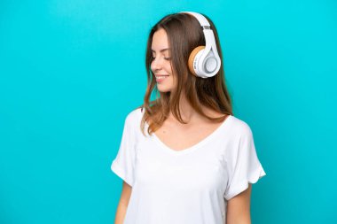 Genç beyaz kadın mavi arka planda izole edilmiş müzik dinliyor.