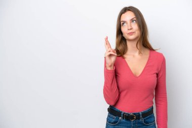 Beyaz arka planda izole edilmiş beyaz tenli genç bir kadın parmaklarını çapraz yapıp en iyisini diliyor.