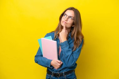 Genç beyaz kadın, sarı arka planda izole edilmiş, yukarı bakarken şüpheleri var.