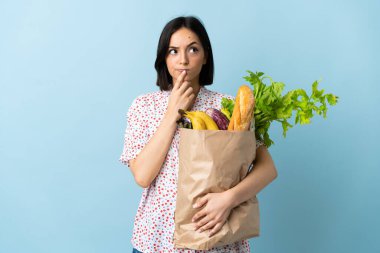 Alışveriş torbası tutan genç bir kadın yukarı bakarken şüphe duyuyor.