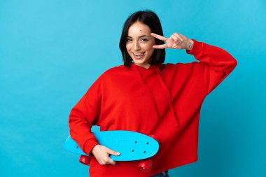 Kafkasyalı genç bir kadın mavi arka planda izole edilmiş mutlu bir ifadeyle paten kayıyor.