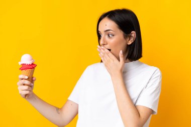 Kornet dondurması olan beyaz bir kadın sarı arka planda, şaşırmış ve şok olmuş bir yüz ifadesiyle izole edilmiş.