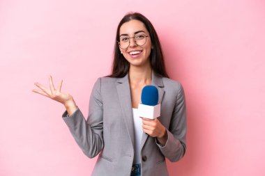 Pembe arka planda izole edilmiş beyaz TV sunucusu genç kadın davet edildiği için ellerini yana uzatıyor.