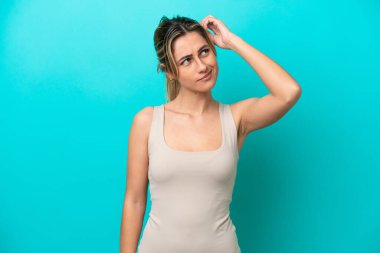 Kafkasyalı genç bir kadın mavi arka planda izole edilmiş. Kafasını kaşırken şüpheleri var.