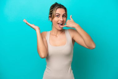 Kafkasyalı genç bir kadın mavi arka planda izole edilmiş telefon jestleri yapıyor.