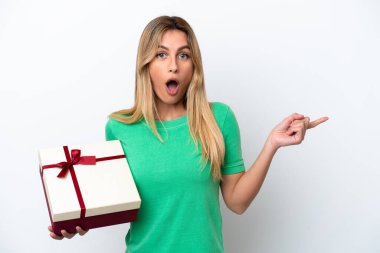 Genç Uruguaylı kadın elinde beyaz arka planda izole edilmiş bir hediye tutuyor. Şaşırmış ve işaret ediyor.