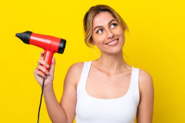 Genç Uruguaylı kadın elinde saç kurutma makinesiyle Don sarı arka planı izole ediyor gülümserken yukarı bakıyor