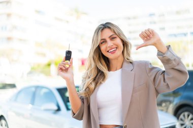 Güzel sarışın Uruguaylı kadın dışarıda arabanın anahtarlarını tutuyor gururlu ve kendinden memnun.
