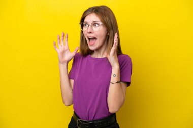 Sarı arka planda yalıtılmış genç bir İngiliz kadın. Sürpriz bir yüz ifadesi var.