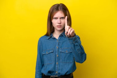 Sarı arka planda izole edilmiş genç İngiliz kadın ciddi bir ifadeye sahip birini sayıyor.