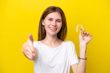 Görünmez diş tellerini tutan genç İngiliz kadın iyi bir anlaşma için el sıkışıyor.