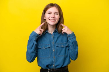 Sarı arka planda izole edilmiş genç bir İngiliz kadın baş parmak işareti yapıyor.
