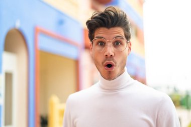 Açık havada genç beyaz bir adam gözlüklü ve şaşırmış bir ifadeyle