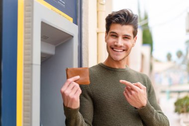 Açık havada ATM kullanan genç beyaz bir adam.