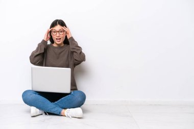 Dizüstü bilgisayarı olan genç bir kadın yerde oturuyor. Sürpriz bir ifadeyle.