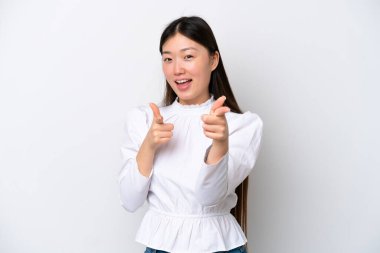 Beyaz arka planda izole edilmiş genç Çinli kadın şaşırmış ve ön tarafı işaret ediyor.