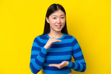 Sarı arka planda izole edilmiş genç bir Çinli kadın bir ilan vermek için avucunun içinde hayali bir fotokopi makinesi tutuyor.