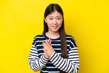 Sarı arka planda izole edilmiş genç Çinli bir kadın bir konferanstan sonra alkışlıyor.