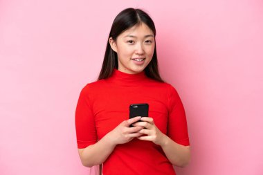 Pembe arka planda izole edilmiş genç bir Çinli kadın cep telefonuyla mesaj gönderiyor.