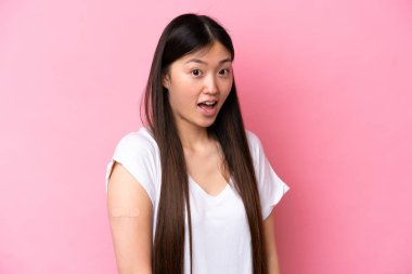 Pembe arka planda yara bandı takan genç Çinli kadın şaşırmış ve şok olmuş bir yüz ifadesiyle izole edilmiş.