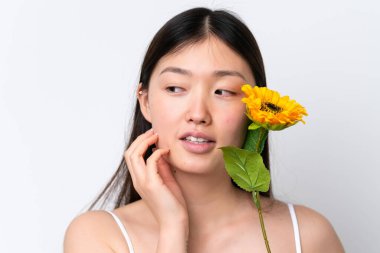 Beyaz arka planda izole edilmiş genç bir Çinli kadın gülümserken elinde bir ayçiçeği tutuyor. Portreyi kapat