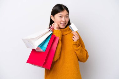Beyaz arka planda izole edilmiş genç bir Çinli kadın elinde alışveriş çantaları ve bir kredi kartı tutuyor.