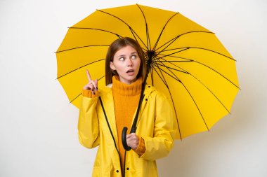 Yağmura dayanıklı ceketi ve şemsiyesi olan genç bir İngiliz kadını beyaz arka planda izole edilmiş.