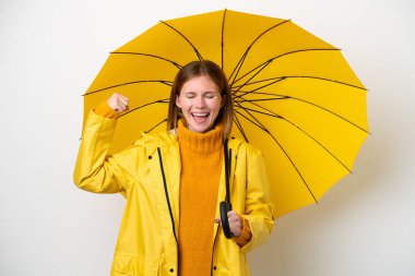 Yağmura dayanıklı ceketi ve şemsiyesi olan genç bir İngiliz kadın beyaz arka planda güçlü bir jest yapıyor.