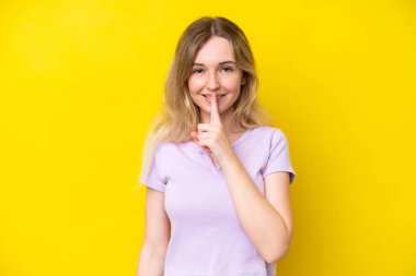 Sarışın İngiliz genç kız sarı arka planda izole edilmiş. Sessiz bir jest işareti var. Parmağını ağzına sok.
