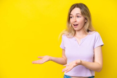 Sarışın İngiliz genç kız, sarı arka planda yalıtılmış, sürpriz bir ifadeyle yan yana bakarken.