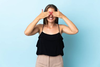 Young Uruguayan woman isolated on blue background covering eyes by hands and smiling