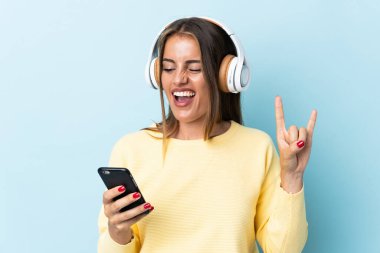 Genç Uruguaylı bir kadın mavi arka planda izole edilmiş, hareketli bir rock hareketi yaparak müzik dinliyor.