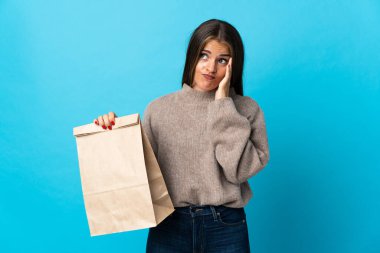 Bir çanta yiyecek alan bir kadın mavi arka planda izole edilmiş bir fikir düşünüyor.